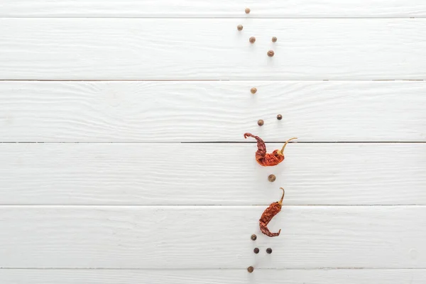 Vista superior de pimienta negra dispersa y chiles secos en mesa de madera blanca - foto de stock