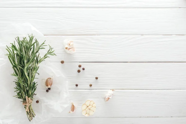 Top view of garlic cloves, black pepper and rosemary on white wooden table — Stock Photo