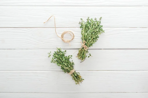 Top view of green thyme near thread on white wooden table — Stock Photo