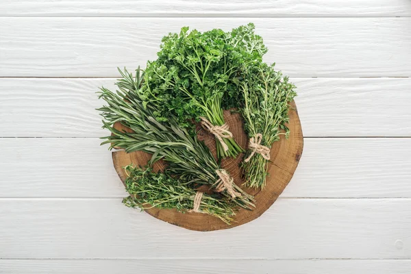 Top view of green parsley, rosemary and thyme on brown stump on white wooden table — Stock Photo