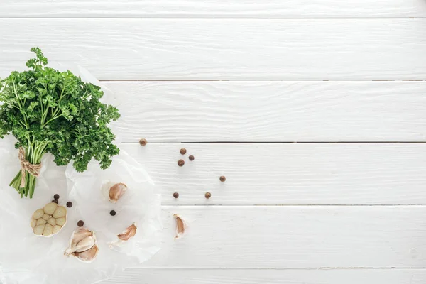 Ansicht von Knoblauchzehen, schwarzem Pfeffer und Petersilie auf weißem Holztisch — Stockfoto