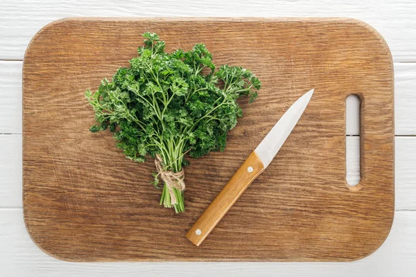 Vue du dessus du persil vert et du couteau sur planche à découper en bois — Photo de stock