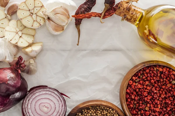 Top view of garlic cloves, red onion, coriander and pink peppercorn in bowls on white paper background — Stock Photo