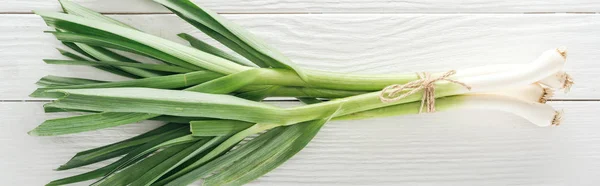 Top view of fresh green leek on white wooden table, panoramic shot — Stock Photo