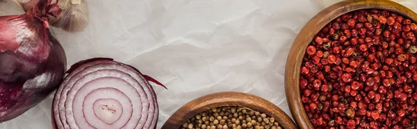 Panoramic shot of red onion, coriander and pink peppercorn in bowls on white paper background — Stock Photo
