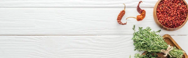 Plan panoramique de piments secs, poivre rose dans un bol près de la planche avec thym sur table en bois blanc — Photo de stock