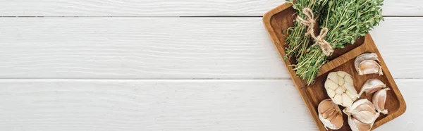 Panoramic shot of board with garlic cloves and thyme on white wooden table — Stock Photo