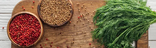 Panoramic shot of coriander and pink peppercorn in bowls near green dill on wooden chopping board — Stock Photo