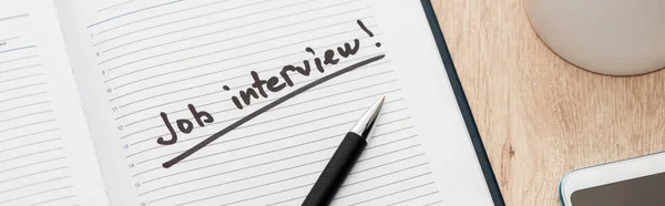 Panoramic shot of job interview lettering in notebook with pen on wooden table — Stock Photo