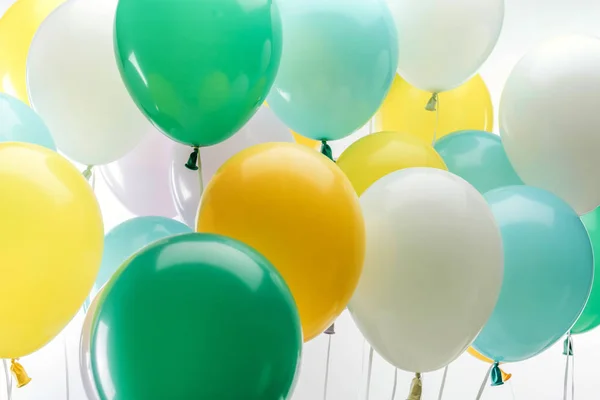 Vista de cerca de globos decorativos de color verde brillante, amarillo y azul sobre fondo blanco - foto de stock