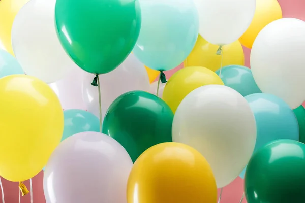 Vista de cerca de globos decorativos de color verde brillante, blanco, amarillo y azul sobre fondo rosa - foto de stock