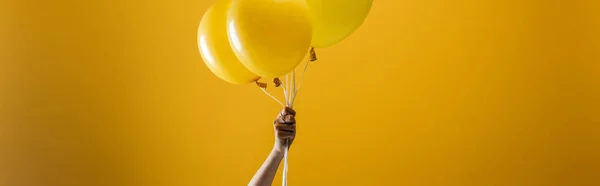 Cropped view of woman holding festive bright minimalistic decorative balloons on yellow background, panoramic shot — Stock Photo