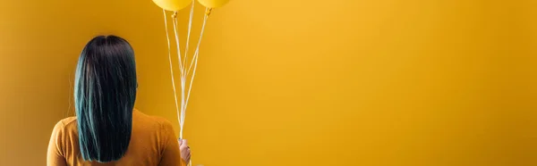 Back view of woman holding festive bright balloons on yellow background, panoramic shot — Stock Photo