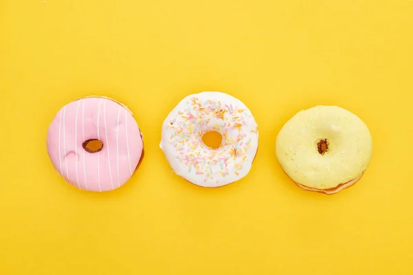 Vista superior de saborosos donuts vidrados coloridos no fundo amarelo brilhante — Fotografia de Stock