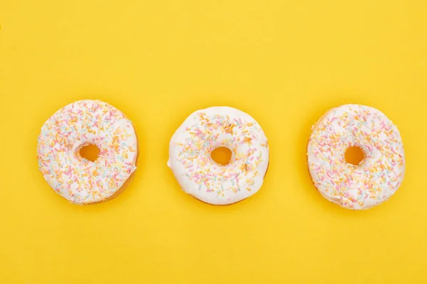 Draufsicht auf leckere glasierte Donuts mit Streusel auf leuchtend gelbem Hintergrund — Stockfoto