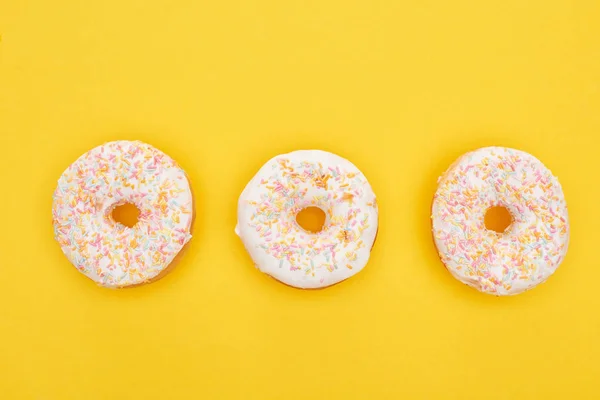 Vista superior de sabrosas rosquillas acristaladas con salpicaduras sobre fondo amarillo brillante - foto de stock