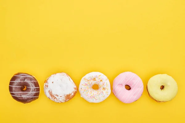 Vista superior de saborosos donuts envidraçados no fundo amarelo brilhante — Fotografia de Stock