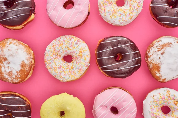 Вид сверху на вкусные глазурованные красочные пончики на ярко-розовом фоне — стоковое фото
