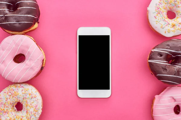 Vista superior de saborosos donuts envidraçados e smartphone com tela em branco no fundo rosa brilhante — Fotografia de Stock