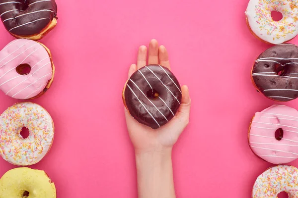 Partial view of woman holding chocolate doughnut on bright pink background — Stock Photo