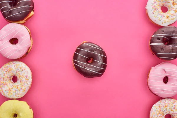 Top view of tasty chocolate doughnut among glazed another on bright pink background — Stock Photo