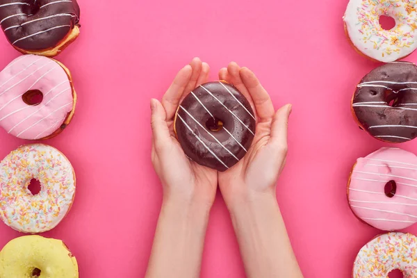 Visão parcial da mulher segurando donut de chocolate nas mãos sobre fundo rosa brilhante — Fotografia de Stock