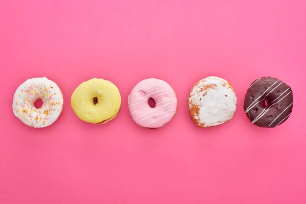 Flache Lage mit leckeren glasierten Donuts auf leuchtend rosa Hintergrund — Stockfoto
