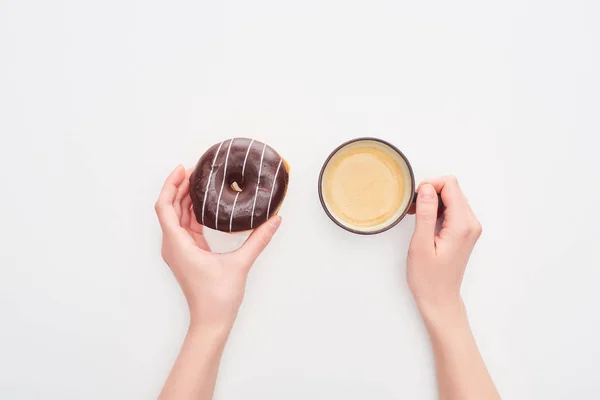 Обрезанный вид женщины, держащей вкусный шоколадный пончик с глазурью и чашку кофе на белом фоне — стоковое фото
