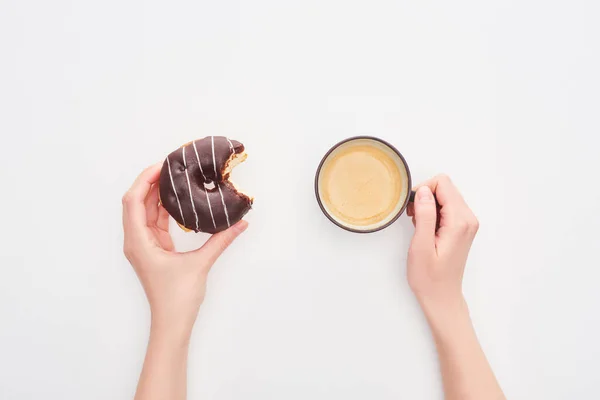 Cropped view of woman holding tasty glazed bitten chocolate doughnut and coffee cup on white background — Stock Photo