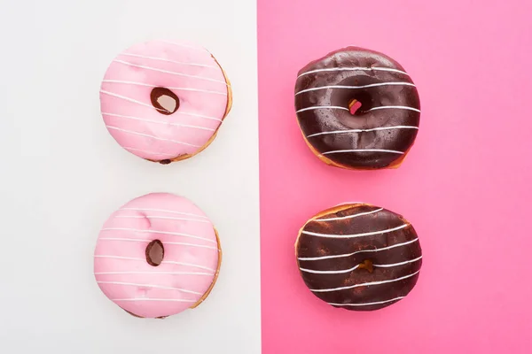 Vista superior de rosa envidraçado e donuts de chocolate no fundo colorido branco e rosa — Fotografia de Stock