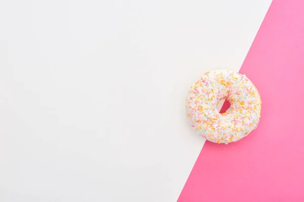 Top view of glazed white doughnut with sprinkles on white and pink background with copy space — Stock Photo