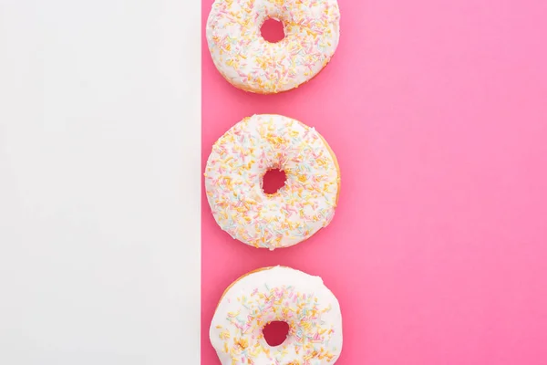 Vista superior de donuts envidraçados com polvilhas sobre fundo branco e rosa — Fotografia de Stock