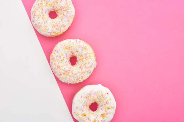 Vista dall'alto di gustose ciambelle smaltate su sfondo bianco e rosa con spazio copia — Foto stock