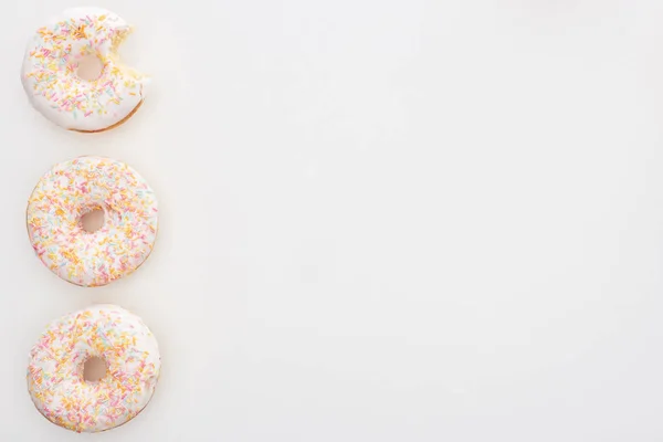 Vista superior de saborosos donuts inteiros com polvilhas perto mordido um no fundo branco — Fotografia de Stock