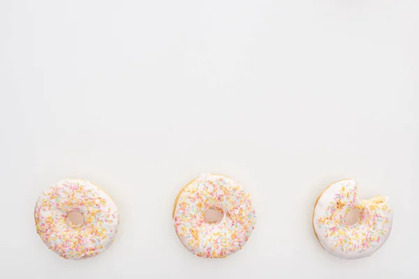 Top view of sweet whole doughnuts with sprinkles near bitten one on white background — Stock Photo