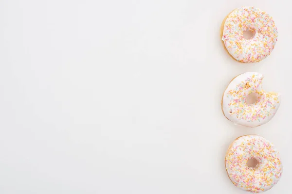 Vista superior de donuts inteiros com polvilhas perto mordido um no fundo branco — Fotografia de Stock