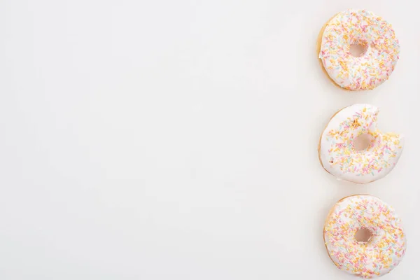 Vue de dessus de beignets entiers avec des aspersions près mordu un sur fond blanc — Photo de stock