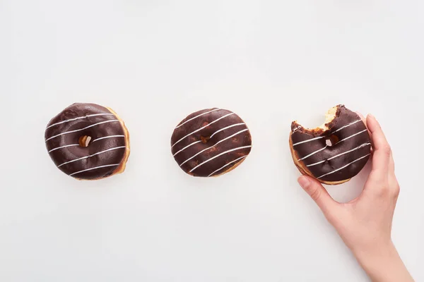 Partial view of woman holding glazed chocolate bitten doughnut on white background — Stock Photo