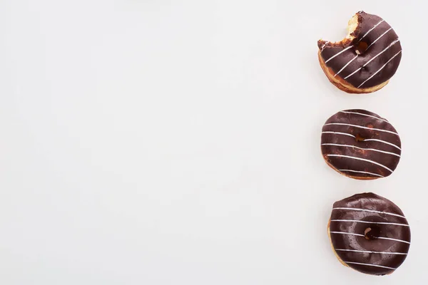 Top view of chocolate tasty whole doughnuts near bitten one on white background with copy space — Stock Photo