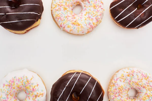 Vista superior de chocolate vidros e donuts brancos com polvilhas sobre fundo branco — Fotografia de Stock