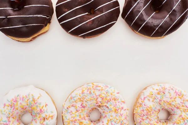 Вид сверху на вкусные шоколадные глазурованные и белые пончики с брызгами на белом фоне — стоковое фото