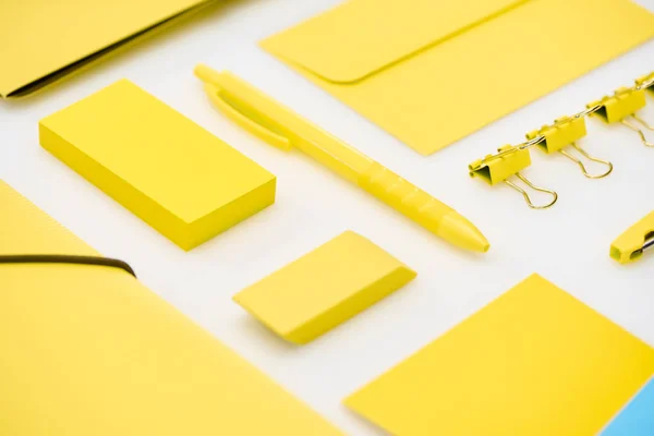 Pose plate de stylo jaune, autocollants, trombones, dossiers, gomme et enveloppe sur fond blanc — Photo de stock
