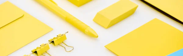 Plano panorámico de lápiz amarillo, clips de papel, goma de borrar, pegatinas y sobre sobre fondo blanco - foto de stock