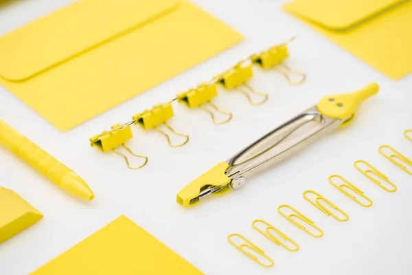 Вибірковий фокус жовтих паперових кліпів, компасів, конвертів, ручки та гумки на білому тлі — стокове фото