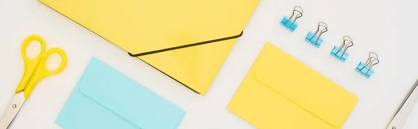 Panoramic shot of yellow and blue envelopes, folders, blue paper clips and yellow scissors isolated on white — Stock Photo