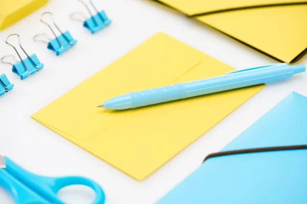 Blue scissors, paper clips, folder and pen on yellow envelope near yellow folder on white background — Stock Photo