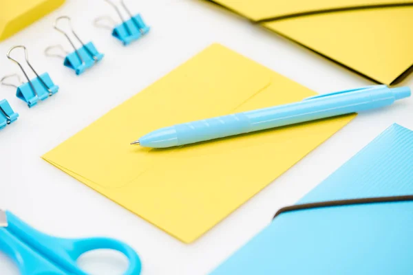 Tijeras azules, clips de papel, carpeta y pluma sobre sobre amarillo cerca de carpeta amarilla sobre fondo blanco - foto de stock