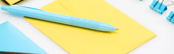 Tiro panorâmico de pasta azul, clipes de papel e caneta no envelope amarelo no fundo branco — Fotografia de Stock
