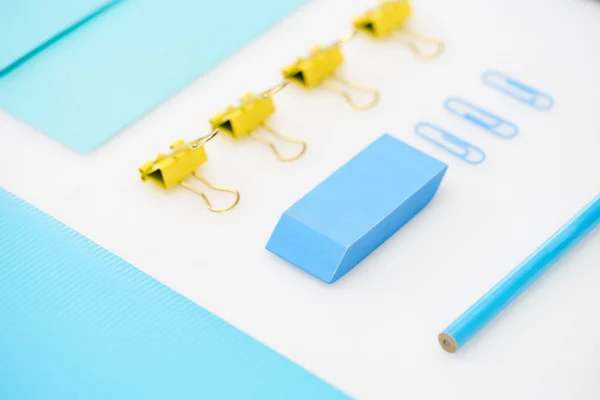 Flat lay of blue paper clips, eraser, folder, pencil, envelope and yellow paper clips — Stock Photo