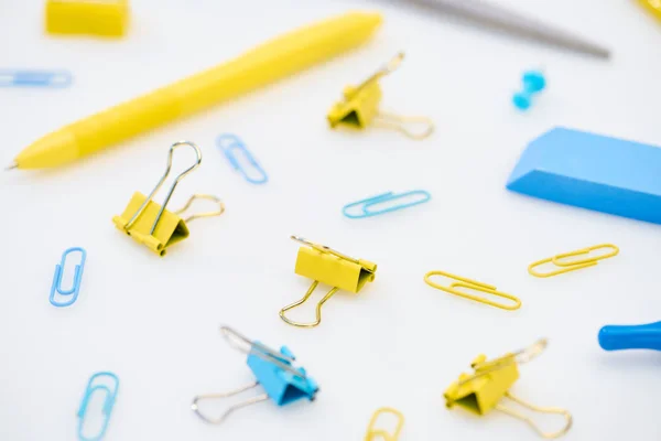 Mise au point sélective de trombones jaunes et bleus avec stylo, gomme, ciseaux et taille-crayon sur fond blanc — Photo de stock
